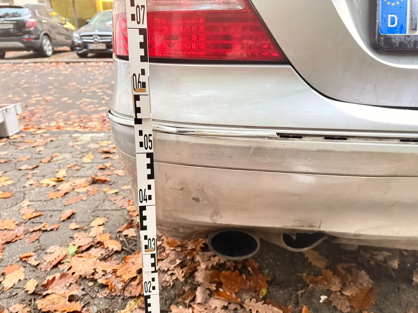 Eingedrückter Heckstoßfänger eines silbernen Autos, daneben ein Messstab