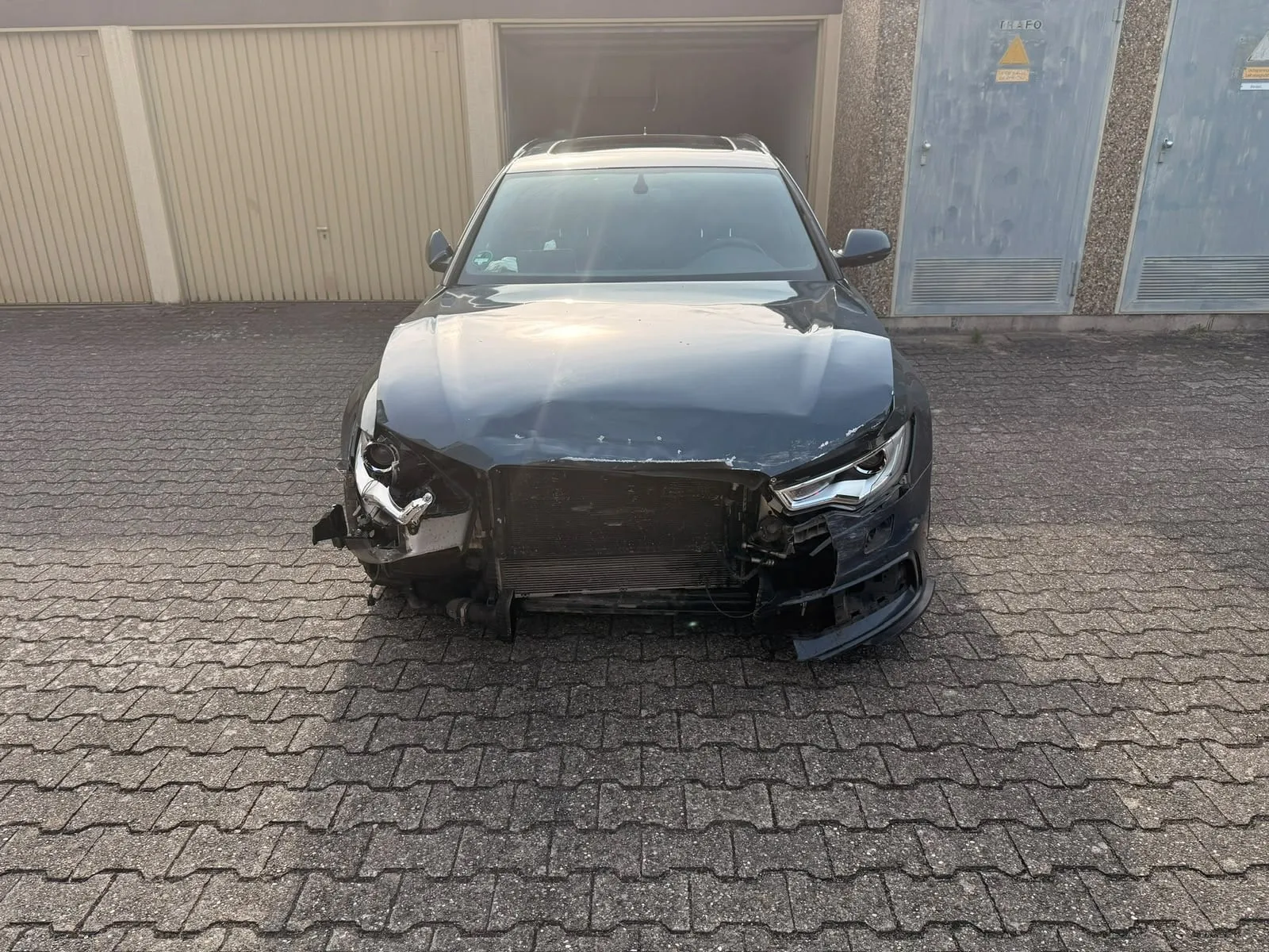 Schwarzer Wagen mit zerstörter Front vor einer Garagenreihe
